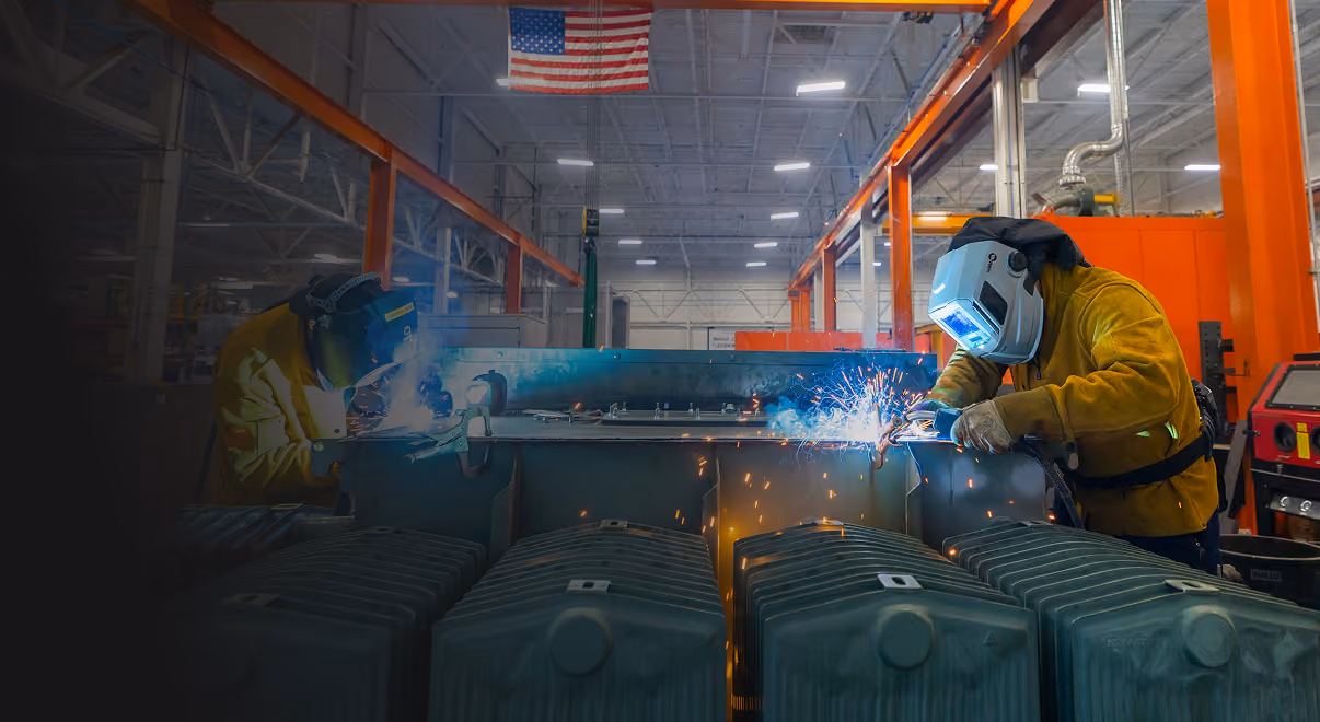 Two welders in yellow jackets welding a Maddox pad mounted transformer