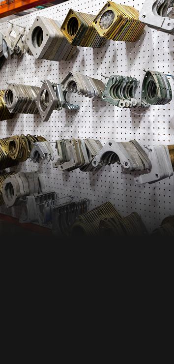 Various metal transformer parts hanging on a white pegboard wall organized in rows.